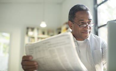 Senior man with newspaper using laptop